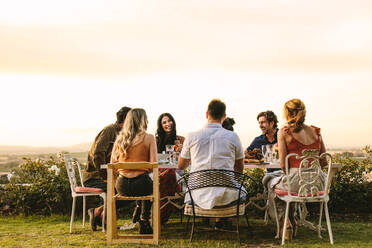 Eine Gruppe junger Freunde sitzt um einen Tisch im Garten und isst zu Abend. Junge Männer und Frauen feiern eine Party im Freien. - JLPSF18947