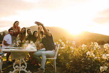 Mann mit Freunden, der ein Selfie mit seinem Smartphone macht. Gruppen-Selfie bei einer Dinnerparty im Freien. - JLPSF18950