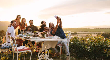 Gruppe von Freunden, die ein Selfie mit einem Smartphone auf einer Dinnerparty machen. Junge Leute auf einer Dinnerparty im Garten, die ein Selfie machen. - JLPSF18952