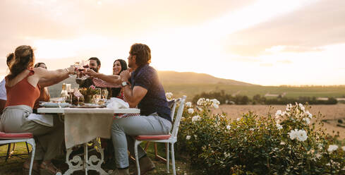 Eine Gruppe von Freunden stößt bei einem Abendessen im Freien mit Weingläsern an. Junge Leute genießen es, beim Abendessen im Garten zu trinken. - JLPSF18953