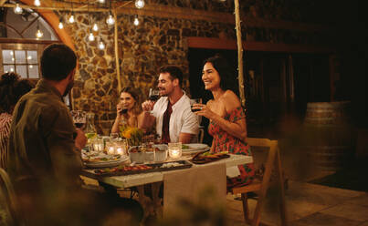 Eine Gruppe von Freunden trinkt Wein bei einer Dinnerparty. Junge Leute haben sich an einem Tisch mit Essen und Getränken versammelt, um einen besonderen Anlass zu feiern. - JLPSF18966