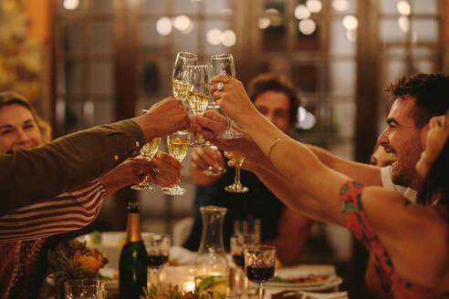 Eine Gruppe von Menschen stößt mit Getränken auf einer Party an. Junge Freunde trinken, um einen besonderen Anlass zu feiern. - JLPSF18970