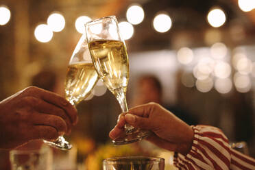 Paar stößt mit Champagnergläsern auf einer Party an. Nahaufnahme eines Mannes und einer Frau, die sich mit Weingläsern auf einer Nachtparty zuprosten. - JLPSF18973