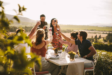 Freunde feiern eine große Party im Freien. Eine Gruppe von Menschen stößt während einer Dinnerparty mit Wein an. - JLPSF18988