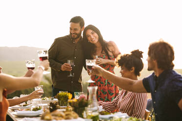 Beautiful young couple being greeting by friends on their pregnancy during a party. Group of friends raising a toast for pregnant couple at dinner party. - JLPSF18997