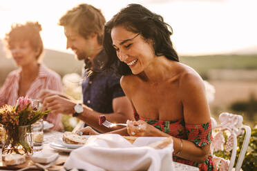 Schöne Frau beim Essen mit Freunden auf einer Party im Freien sitzend. Frau genießt das Essen mit Freunden auf einer Party. - JLPSF19004
