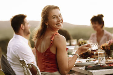 Beautiful woman having food with friends sitting by at dinner party. Woman eating food at outdoor party with friends. - JLPSF19007