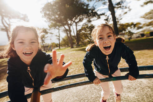 Zwei kleine Zwillinge spielen zusammen auf einem Spielplatz im Freien. Eineiige Zwillinge haben Spaß im Freien, schauen in die Kamera und lachen. - JLPSF19011