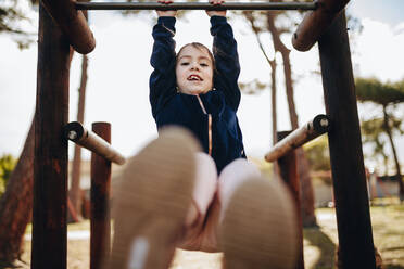 Porträt eines süßen kleinen Mädchens, das an einem Metallrahmen hängt und schaukelt. Junges Mädchen spielt auf dem Spielplatz. - JLPSF19013