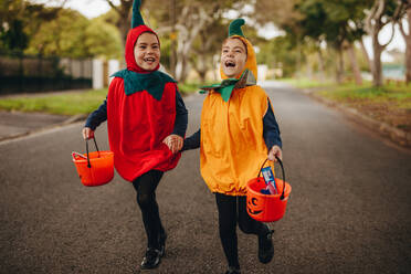 Fröhliche Kinder in Halloween-Kostüm Trick oder Behandlung im Freien. Zwei kleine Mädchen in Halloween-Kostüm mit Eimer zu Fuß im Freien auf der Straße. - JLPSF19033