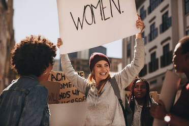 Eine Gruppe von Aktivistinnen protestiert auf der Straße für die Stärkung der Rolle der Frau. Eine lächelnde junge Frau hält ein Transparent während eines Protestes. - JLPSF19049