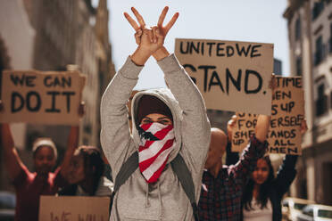 Frau mit verdecktem Mund, die mit beiden Händen auf der Straße ein Friedenszeichen macht. Eine Gruppe von Frauen protestiert schweigend auf der Straße. - JLPSF19058