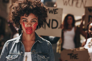 African woman with red colored hand on her mouth during a protest. Group of female activist demonstrating to stop women abuse. - JLPSF19079