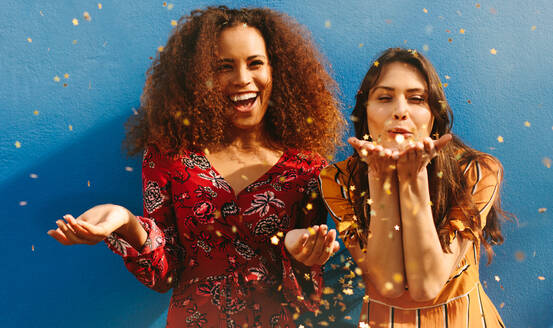 Attraktive junge Frauen blasen Glitter vor blauem Hintergrund. gemischte Rasse weibliche Freunde, die Spaß mit Glitter. - JLPSF19114