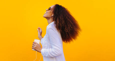 Seitenansicht einer Frau, die Kopfhörer trägt, um Musik von ihrem Mobiltelefon zu hören. Afrikanisches Mädchen, das Spaß hat, während es Musik auf seinem Smartphone hört. - JLPSF19138