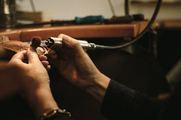 Reife Juwelierin, die einen Goldring an der Werkbank poliert. Goldschmiedin, die einen Ring in ihrer Werkstatt mit Werkzeugen herstellt. Nahaufnahme der Hände einer Juwelierin, die eine Poliermaschine benutzt. - JLPSF19145