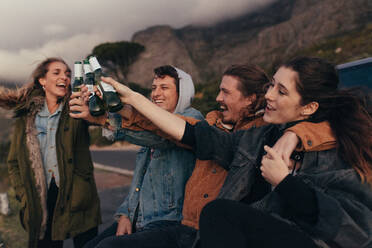 Eine Gruppe von Freunden sitzt auf dem Highway und stößt mit Bierflaschen an. Freunde auf einem Highway-Trip genießen und feiern. - JLPSF19154