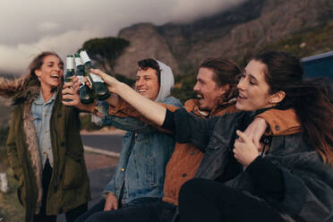 Group of friends sitting on highway toasting bottles of beer. Friends on a highway trip enjoying and partying. - JLPSF19154