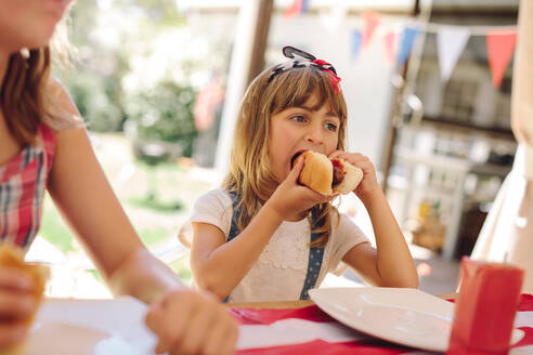 Mädchen isst einen Hotdog im Kreise ihrer Familie. Kleines Mädchen isst einen Hotdog in einem Restaurant. - JLPSF19167