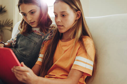 Zwei Mädchen sehen sich zu Hause einen Film auf einem Tablet-PC an. Junge Mädchen sitzen zu Hause zusammen und benutzen einen Tablet-PC, um neue Dinge zu lernen. - JLPSF19184