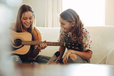 Zwei Mädchen im Teenageralter, die zu Hause zusammensitzen und Spaß am Gitarrenspiel haben. Mädchen, das zu Hause mit ihrer Freundin Gitarre spielen lernt. - JLPSF19185