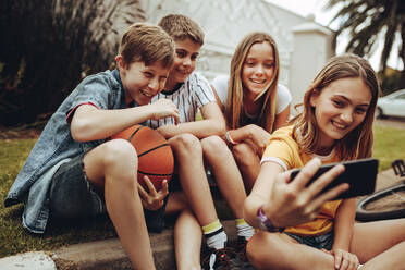 Gruppe von Kindern, die Spaß daran haben, ein Selfie mit dem Handy zu machen. Glückliche Jungen und Mädchen, die am Rande einer Straße sitzen und ein Selfie machen. - JLPSF19192