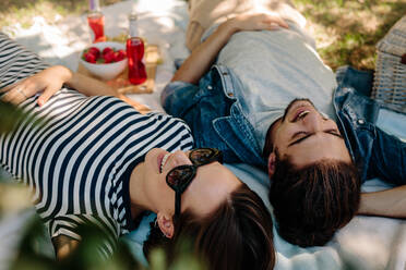 Glücklicher junger Mann und Frau mit Sonnenbrille im Park liegend. Fröhliches Paar beim Picknick in einem Park. - JLPSF19223