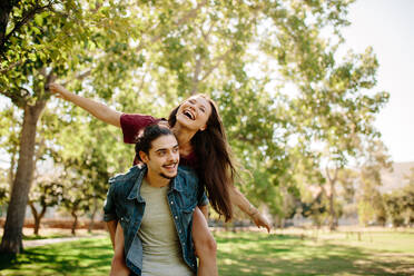 Hübscher junger Mann nimmt seine Partnerin im Park huckepack. Ein Paar genießt einen Sommertag im Park. - JLPSF19241