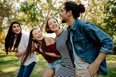 Drei Frauen schauen einen jungen Mann im Park an und lachen. Eine Gruppe von Freunden genießt einen gemeinsamen Spaziergang im Park. - JLPSF19257