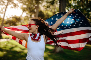 Junge Frau genießt im Park hält USA-Flagge. Amerikanisches Mädchen mit Nationalflagge, die Spaß im Park. - JLPSF19269