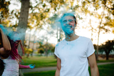 Woman throwing powder paint her boyfriend. Couple playing with colored powder in the park. - JLPSF19285