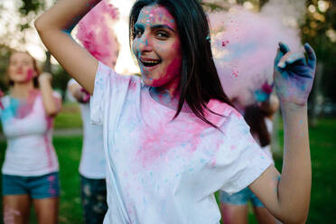 Woman with friends showering paints at the back playing holi in the park. Group of friends playing with color powder outdoors. - JLPSF19288