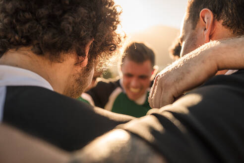 Close up of rugby players standing in a huddle. Group of sportsmen standing in circle after the match focus on hands on shoulders. - JLPSF19305