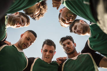 Low angle view of rugby players in circle against clear sky discussing their tactics. Team of rugby player in huddle between the match. - JLPSF19307