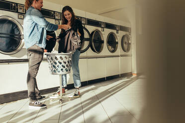 Cheerful couple doing laundry together in a laundry room. Smiling couple washing clothes together in washing machine. - JLPSF19338