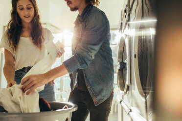 Ein Paar wäscht zusammen Wäsche aus einem Korb. Ein Paar in einer Waschküche wäscht Wäsche mit Sonnenlicht im Hintergrund. - JLPSF19340