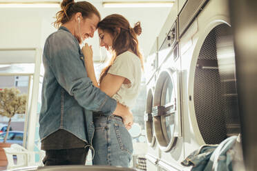 Verliebtes Paar, das zusammen in einer Waschküche steht und sich gegenseitig an der Stirn berührt. Paar, das Musik hört und sich Kopfhörer teilt, steht in einer Waschküche. - JLPSF19346