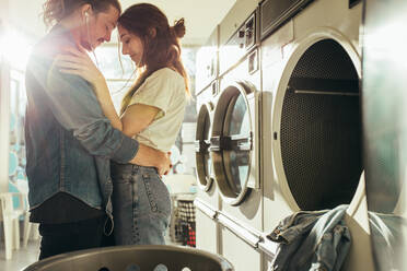 Paar in einer Waschküche, das sich gegenseitig hält und die Stirn berührt. Verliebtes Paar, das sich umarmt und in einer Waschküche steht. - JLPSF19347