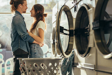 Happy couple sharing earphones listening to music standing in a laundry room. Couple in love standing facing each other with closed eyes. - JLPSF19348