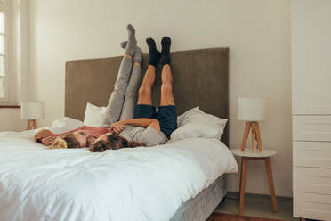 Happy couple lying on bed together holding hands looking at each other. Couple lying on bed with legs raised to the wall and talking. - JLPSF19355