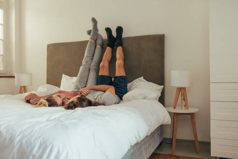 Ein glückliches Paar liegt auf dem Bett und hält sich an den Händen, während es sich gegenseitig anschaut. - JLPSF19355