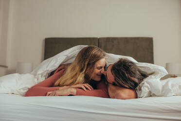 Paar auf dem Bett liegend zu Hause romantisch durch Berühren ihrer Nasen. Glücklicher Mann und Frau auf dem Bett liegend in einer gemütlichen Decke bedeckt verbringen Zeit miteinander. - JLPSF19359