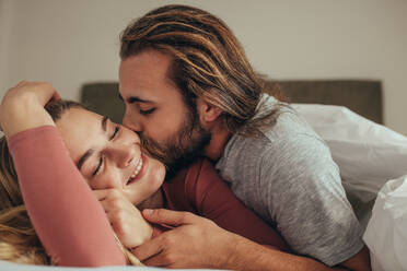 Mann küsst seine Frau, während er auf dem Bett schläft. Paar im Bett, bedeckt mit einer Decke, der Mann küsst seine Partnerin. - JLPSF19361