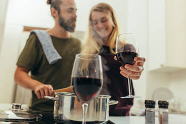 Glückliches Paar beim Kochen in der Küche stehend und ein Glas Wein genießend. Mann hilft seiner Frau bei der Zubereitung des Abendessens zu Hause. - JLPSF19373