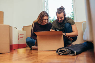 Happy couple opening their items after moving in a new home. Smiling man and woman looking at their articles packed inside a box. - JLPSF19378