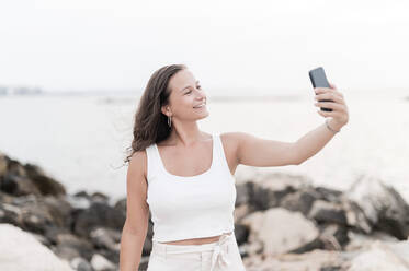 Lächelnde Frau, die im Strandurlaub ein Selfie mit ihrem Smartphone macht - MEF00126