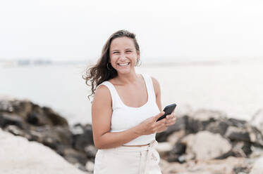 Glückliche junge Frau mit Mobiltelefon im Strandurlaub - MEF00127