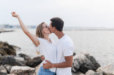 Woman with hand raised kissing boyfriend at beach - MEF00134