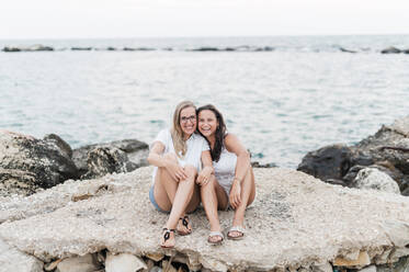 Happy friends sitting together on rock at beach - MEF00136