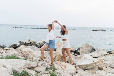 Friends holding hands and walking together on rock at beach - MEF00137